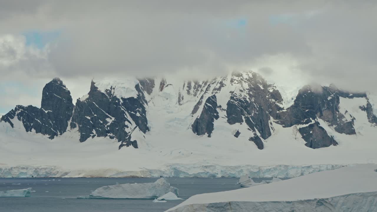 Timelapse dramático de nuvens rolando e se movendo sobre picos montanhosos antárticos rochosos escuros e irregulares acima de uma plataforma de gelo congelada e águas escuras do oceano polar
