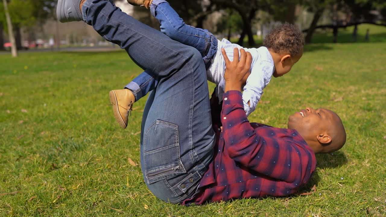 Vater sitzt auf dem Gras, spielt mit dem Jungen, hält ihn in den Armen.