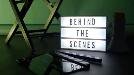 behind the scenes letterboard text on lightbox or cinema light box. movie clapperboard megaphone and director chair beside. background led color change loop. static camera in video production studio.