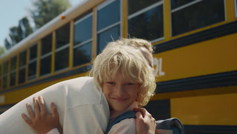 mother meeting son hugging at school bus. smiling boy looking camera close up.