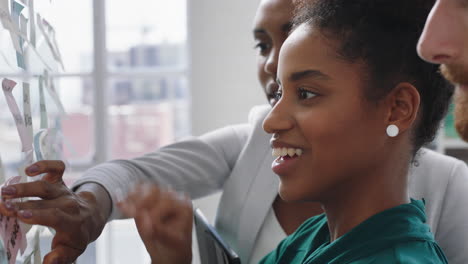 mixed race business woman using sticky notes brainstorming problem solving with colleagues sharing creative ideas for solution in office