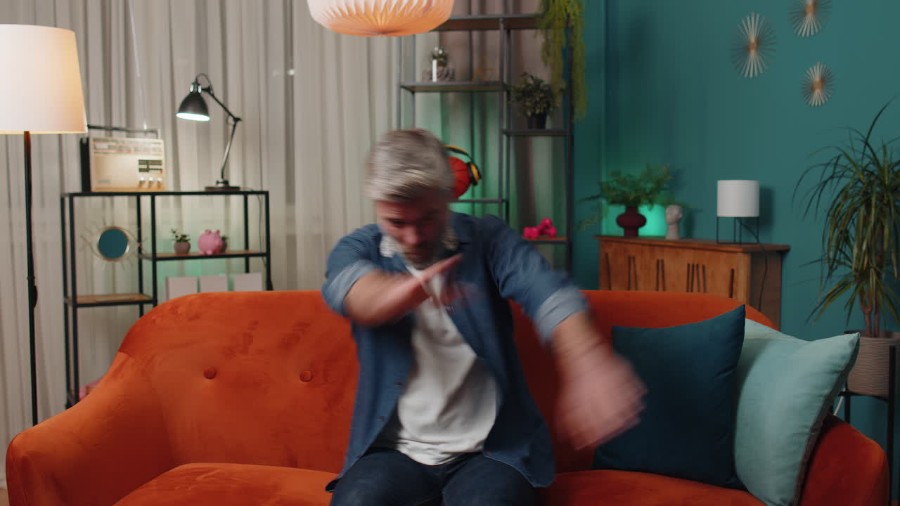 Trendy cheerful mature old man dancing and moving to rhythm making dub dance gesture at modern home