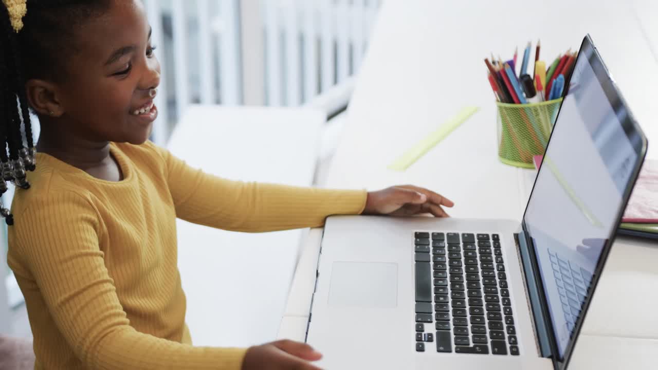 Happy african american girl using laptop raising hand in online class, slow motion
