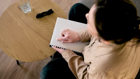 blind woman reading a braille book while sitting on sofa at home