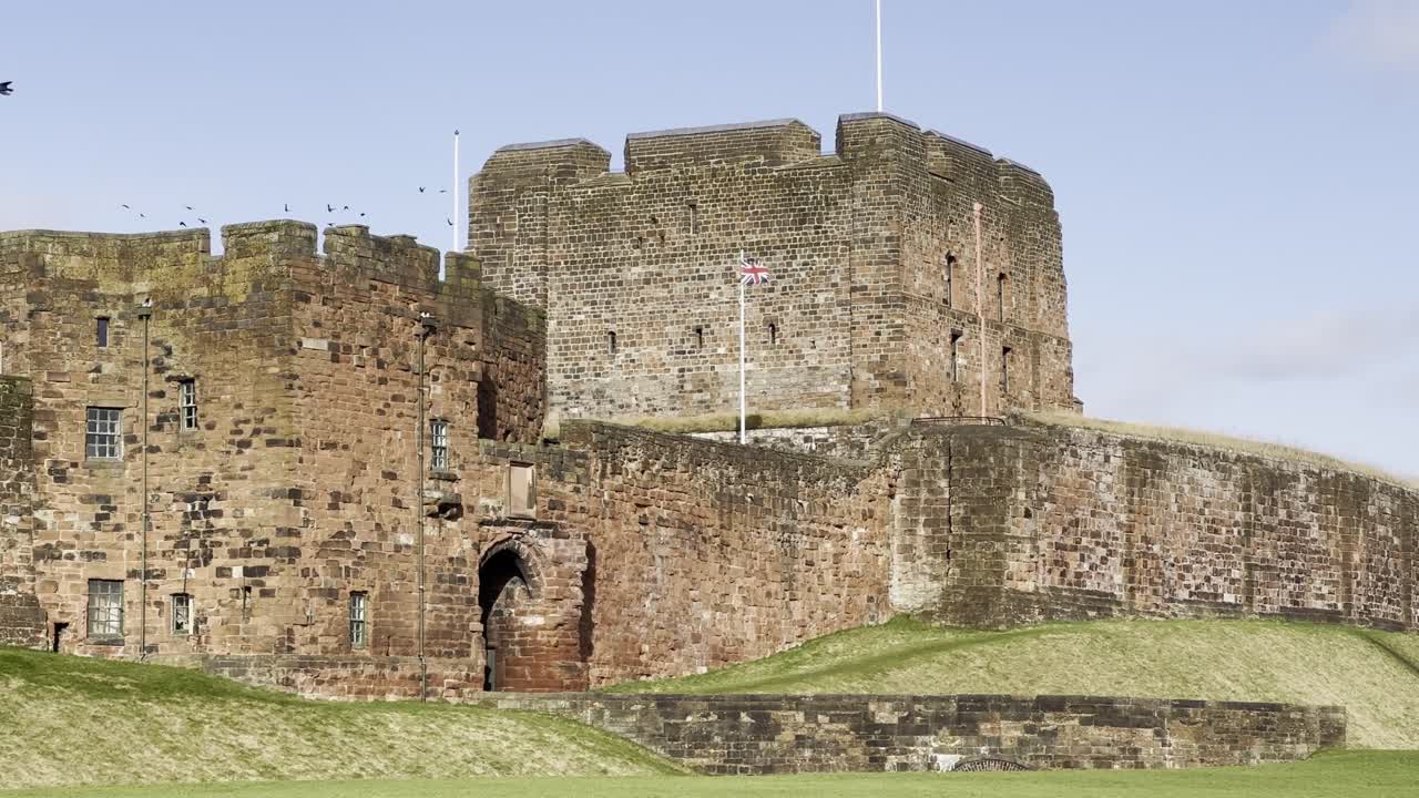 Front entrance of Carlisle Castle with Union Jack waving and flock of birds behind - Cumbria, England