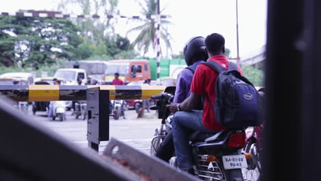 two men on a motorbike wait at a railway crossing in bangalore as a train passes