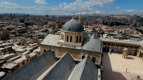 view over the umayyad mosque in syria. drone is flying around the building exterior of a tower mosque and with the city of damascus in the background.