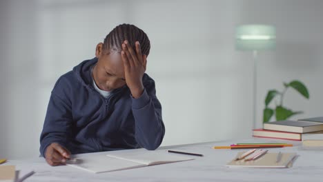 Boy On ASD Spectrum At Table At Home Struggling With Concentrating On Writing In School Book 