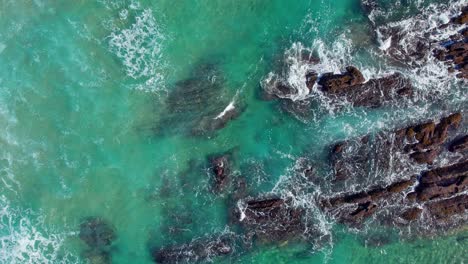 Ocean-waves-on-rock-sediment-stones-from-above,-straight-sea-wave-and-splashing-white-waters,-in-Playa-de-Tagle,-Spanish-coast