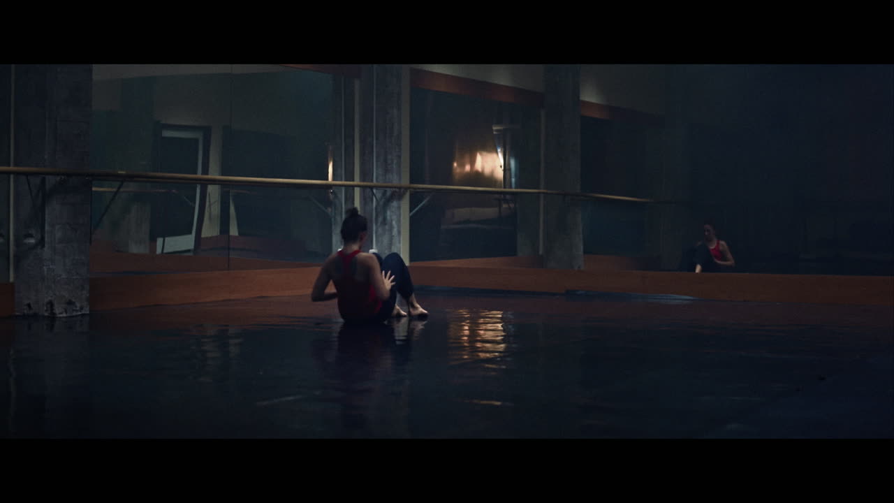 A young woman practices modern dancing and ballet in a moody room full of mirrors