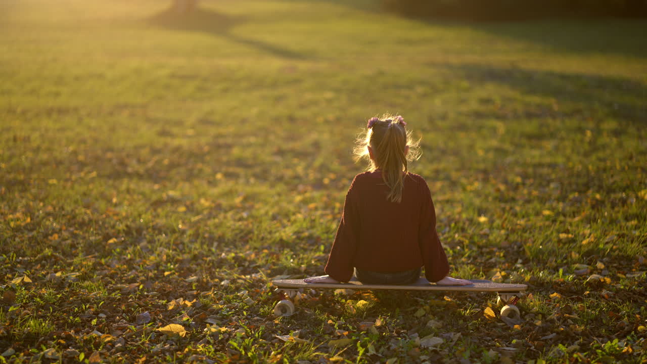 Girl sitting on skateboard in autumn park