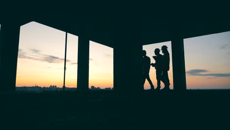 los contratistas caminan en un edificio en un fondo de puesta de sol.