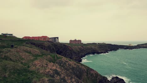 Aerial-drone-footage-flying-over-cliffs-toward-the-Headland-Hotel-in-Newquay,-Cornwall,-UK-with-views-of-the-Atlantic-Ocean