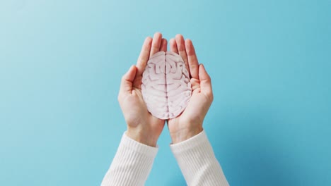 Video-of-hands-holding-brain-on-blue-background-with-copy-space