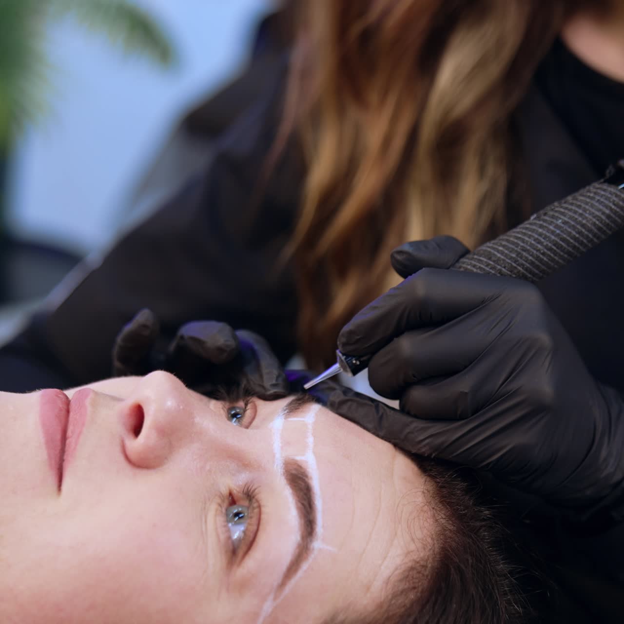 Brow master in black gloves applying special device. Female client having the procedure of permanent make up of eyebrows. Close up