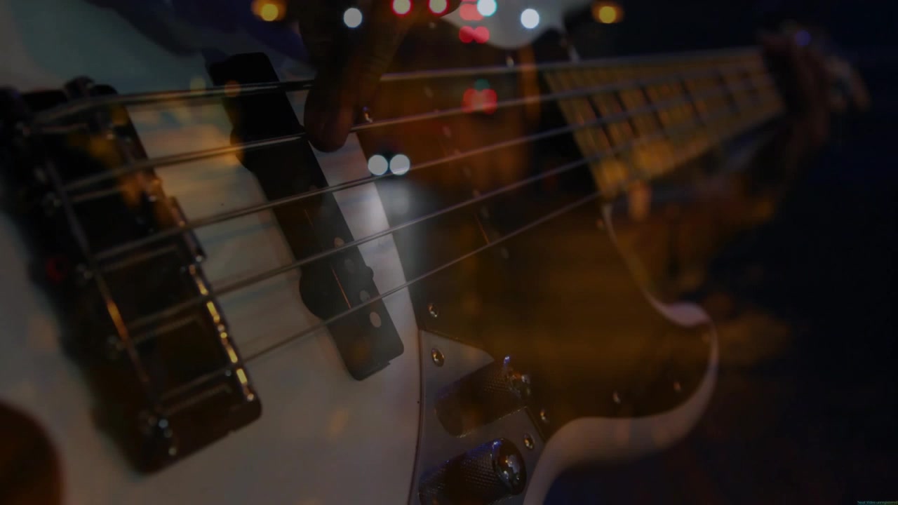 Musicista uomo che pizzica il basso, telecamera che si sposta a destra rivelando le mani, bokeh fantasma che pulsa a ritmo di musica