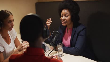 Three-diverse-female-radio-hosts-wearing-headphones-talking-on-microphone-for-radio-podcast