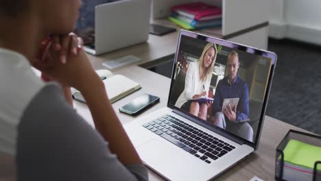 african american woman having a video call with male and female colleagues on laptop at office