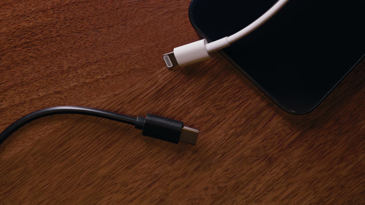 usb-c y un cable relámpago y un teléfono en una mesa de madera con luz en movimiento