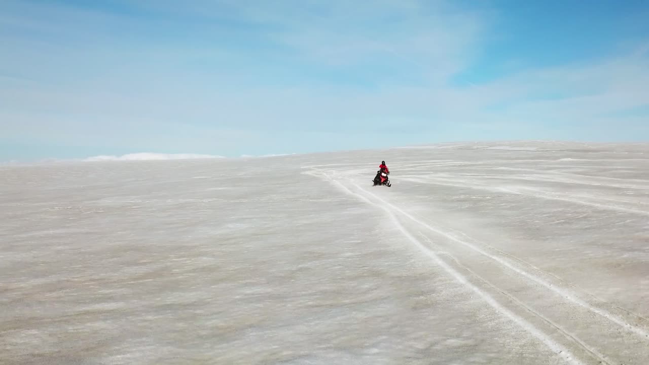 vista aerea di una persona che fa acrobazie su una motoslitta, sulla superficie bianca di un ghiacciaio in islanda, in una giornata di sole