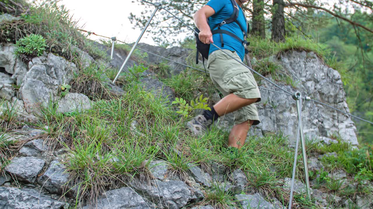 Low angle shot of male hiker descending rocky path holding cable handholds