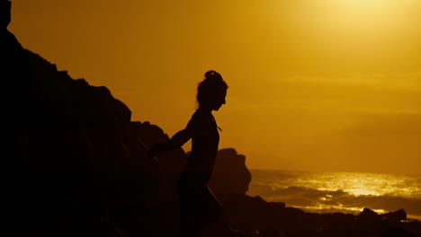 silhouette of a woman at sunrise on a rocky coast
