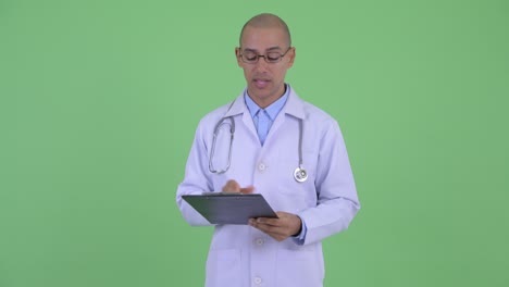 hombre multiétnico calvo y guapo médico con portapapeles