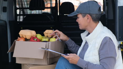 female courier sitting in van and counting products in box