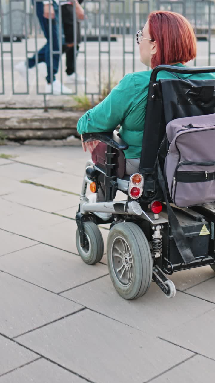 Woman with Red Hair Moving in Electric Wheelchair on City Sidewalk