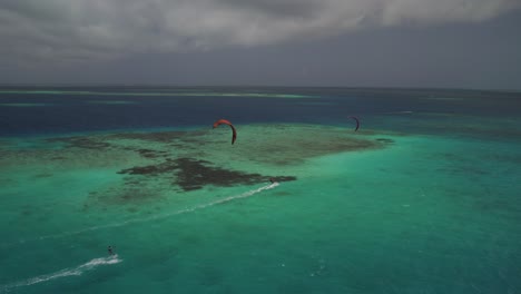 Zwei-Kitesurfer-Gleiten-über-Ein-Lebendiges-Korallenriff-Im-Klaren,-Türkisfarbenen-Wasser,-Luftaufnahme