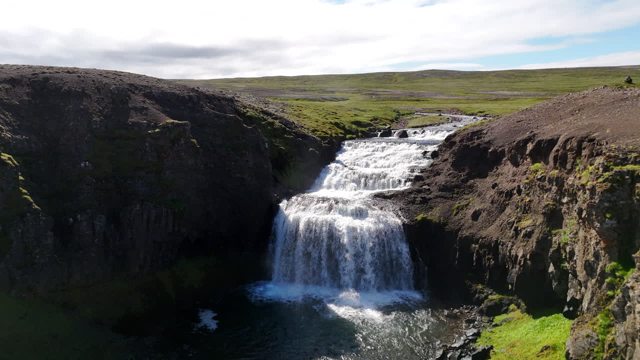 Aerial view of a winding river flowing toward the Greenland Sea in Austurland, Iceland, capturing waterfalls, coastal plains, and open northern landscapes under bright clear skies