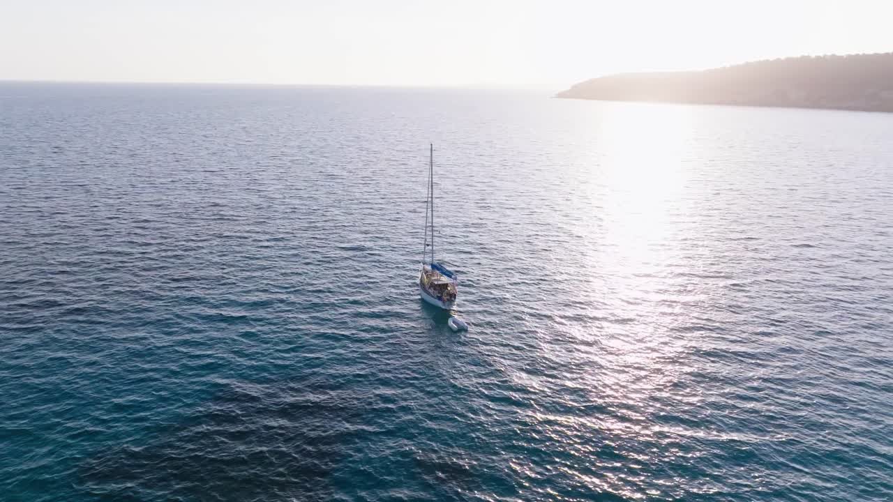 Sailboat catamaran sailing near Menorca island coastline at sunset sun rays water reflection, aerial