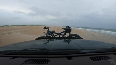 dashboard hyperlapse of an adventure seeking couple traveling along a beach, ocean waves rolling in and dark grey clouds approaching