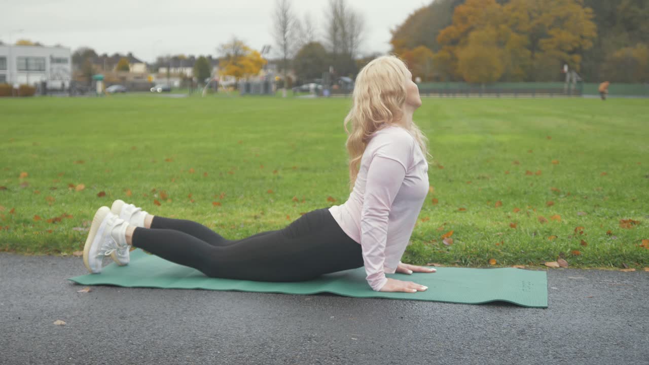 mujer realiza pose de cobra yoga en el parque