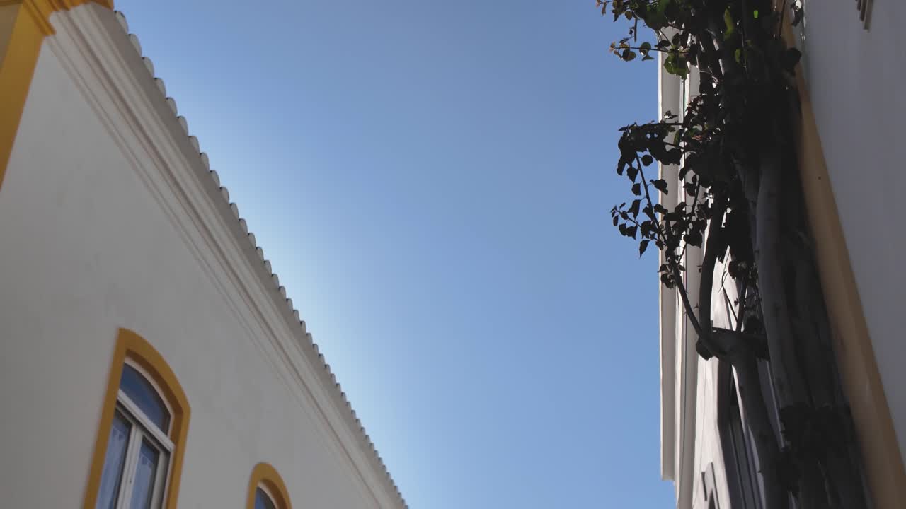 Picturesque narrow cobbled street with charming white buildings adorned with yellow details. tilt down