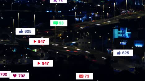 Animation-of-social-media-icons-floating-against-aerial-view-of-night-city-traffic