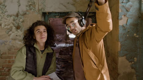 two production coworkers talking while reading a document and holding a microphone during recording of a movie in a ruined building 1