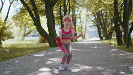 Sport-runner-jogger-child-girl-listen-bluetooth-music-speaker-dancing-to-camera-having-fun-in-park