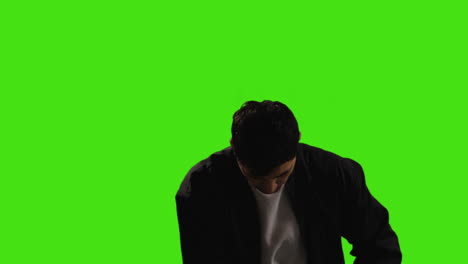 young man answering call on mobile phone standing against green screen studio background with low key lighting