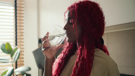 Curly-cheerful-African-American-woman-drinking-glass-of-fresh-water-in-the-morning