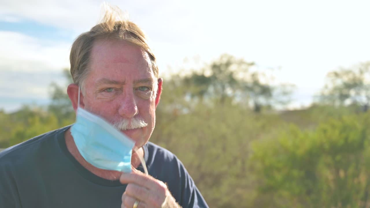 Take off mask end of Covid pandemic concept. Male removes his protective face mask outdoors, breathes fresh air.