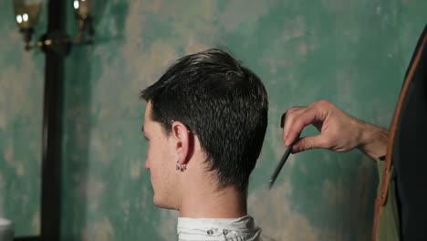 bearded barber in apron combing hair of a male client sitting in the chair at barber shot. slow camera round movement