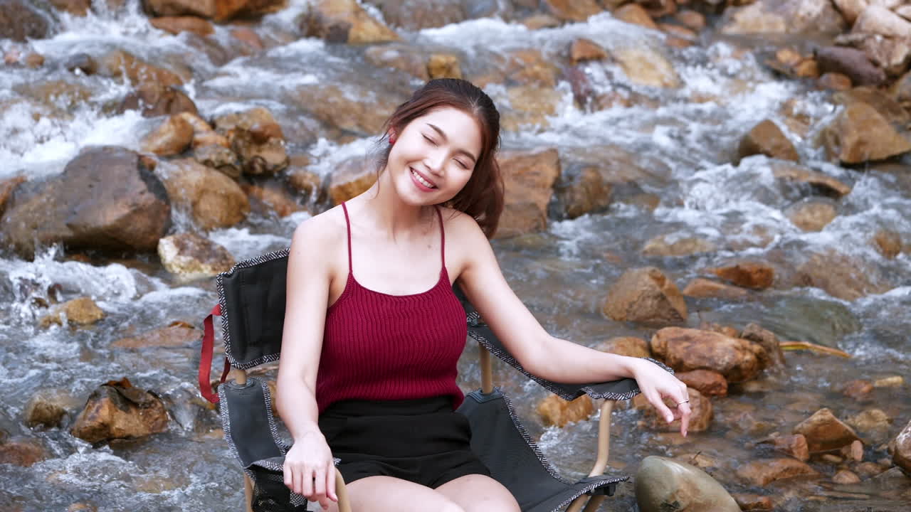 휴가 여름에 휴식과 행복을 위해 큰 바위와 물이 천천히 튀는 의자에 앉아 빨간색으로 아시아 여자