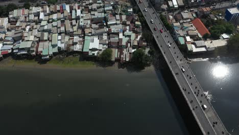 Toma-Aérea-Sobre-Un-Puente-De-Tráfico-Ocupado-Y-Casas-De-Chabolas-Frente-Al-Mar-A-Lo-Largo-Del-Canal-Kenh-Te-En-La-Ciudad-De-Ho-Chi-Minh,-Vietnam-En-Un-Día-Soleado