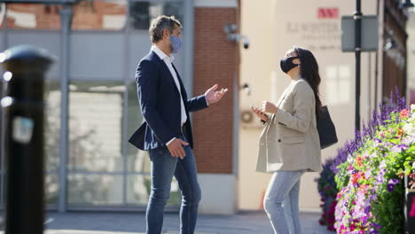 Hombre-De-Negocios-Y-Mujer-De-Negocios-Con-Máscaras-Faciales-Tocándose-Los-Codos-Mientras-Se-Encuentran-En-La-Ciudad