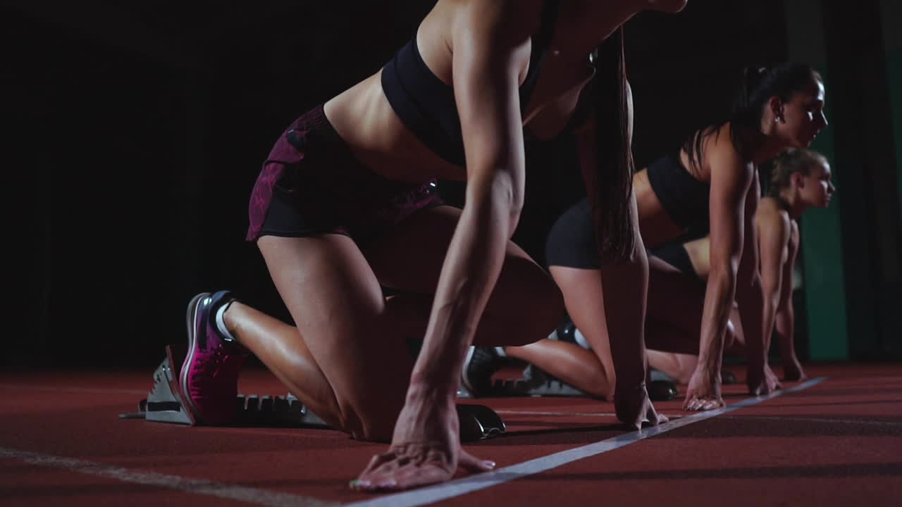 corredoras en la pista de atletismo agachadas en los bloques de salida antes de una carrera. en cámara lenta.