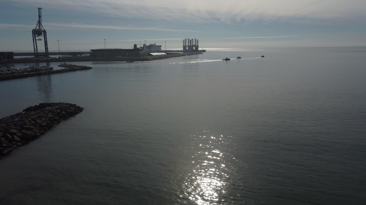 Flying from a beach towards an industrial port entrance. Foggy sunrise.