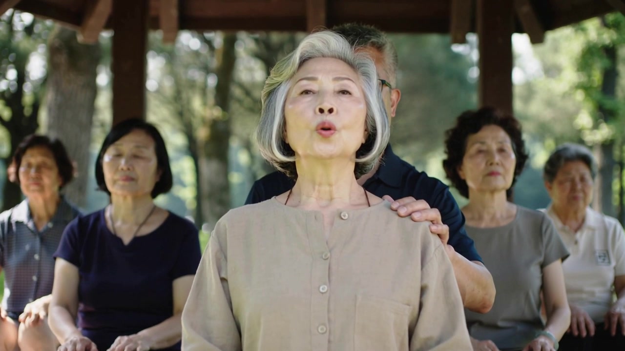 Donna in camicetta che respira con le labbra serrate su una panchina del parco, mentre un uomo le posa le mani sulle spalle durante la lezione.