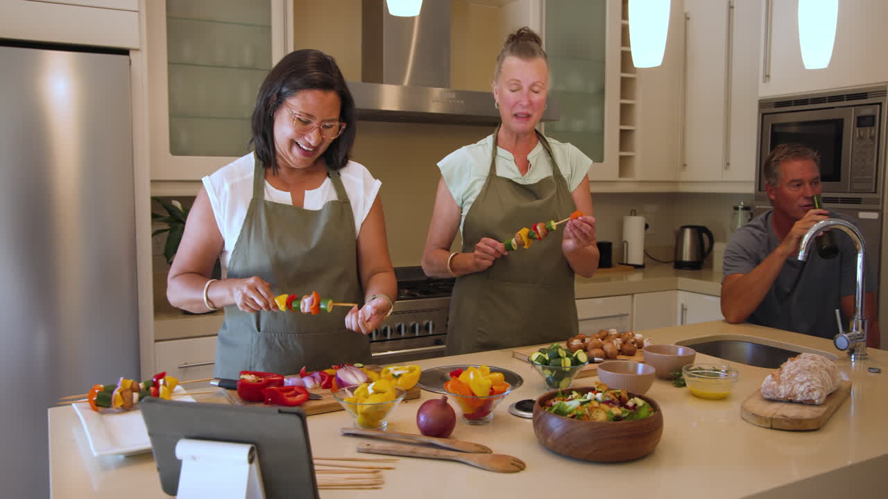 Diverse women preparing colorful vegetable skewers in kitchen, enjoying cooking together, at home