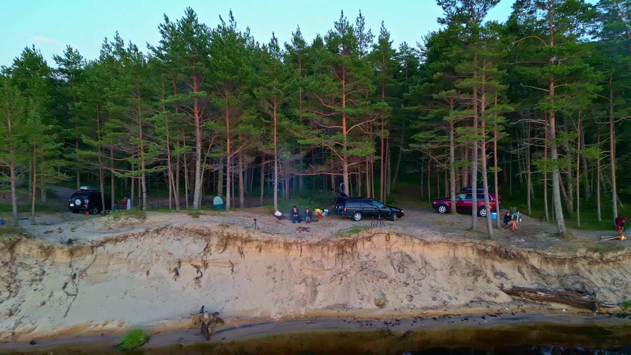 Group camping by a river in a pine forest at dusk
